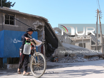 A Syrian boy rides a bike curryin water past destroyed buildings in the rebel-held town of Douma, on the eastern outskirts of the Syrian cap...