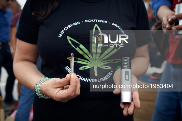 A woman shows to way to smoke cannabis : a joint and a vaporizer. She wears a shirt reading 'inform, support, regulate). For the Global Mari...
