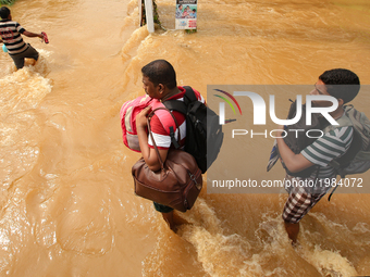 Two Sri Lankan men  walk across a road inundated by floods with their belongings stored in backpacks following Flood warnings issued by gove...
