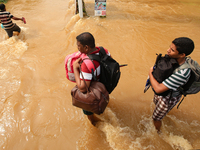 Two Sri Lankan men  walk across a road inundated by floods with their belongings stored in backpacks following Flood warnings issued by gove...
