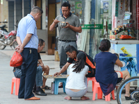 A view of a group of people gathered on the street eating, playing board-games and socialising outside their family businesses and houses in...
