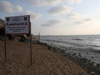 A warning sign reading 'dangerous swimming and fishing' is placed near an outlet flowing sewage into the sea in front in the Shati refugee c...