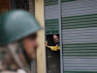 A kashmiri Women peeps out from an half closed shop shutter as an Indian paramilitary stands guard during a curfew  in old city Srinagar  on...