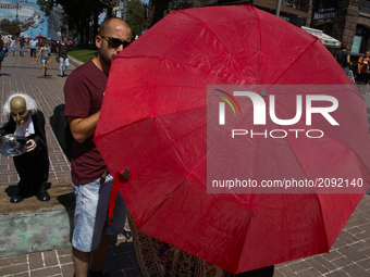 A man talks to a person covered with a red umbrella during a hot day in Kyiv, Ukraine.  (