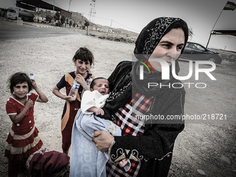 A mother holds her nine-day-old bay named Aara from the sun as she waits with her family at a checkpoint in Badriya where temperatures reach...