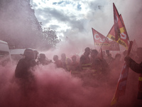 Metalworkers and police officers are surrounded by smoke as they march with banners and flags in the streets of Paris on October 13, 2017. S...