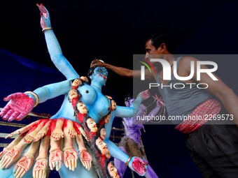 An Indian artist applying colors into the clay idol of goddess Kali at a worship venue on the eve of Kali Puja festival as people offer puja...