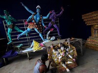An Indian artist applying colors into the clay idol of goddess Kali at a worship venue on the eve of Kali Puja festival as people offer puja...