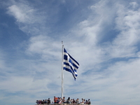 A Greek flag waves as tourists enjoy the view atop of the ancient Acropolis hill in Athens. Greece, Wednesday, October 18, 2017 (