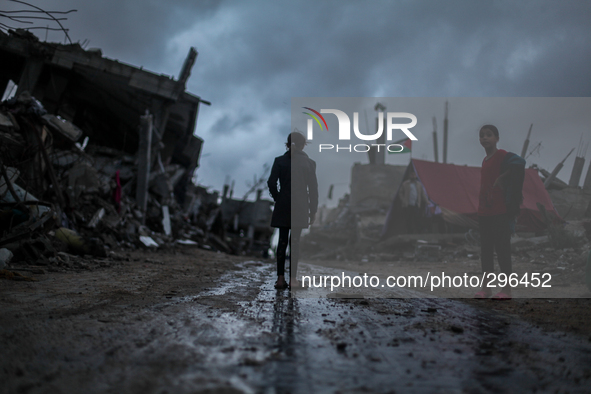 A Palestinian boy looks up during a rain storm while walking through a neighbourhood destroyed during the 50 day conflict between Israel and...