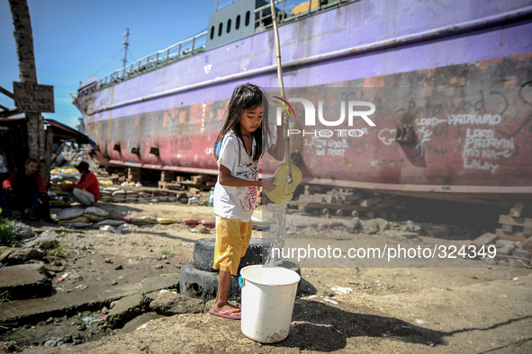 A girl pours water to a bucket next to a ship that was washed ashore at coastal village one year since Typhoon Haiyan hit in Tacloban, Leyte...