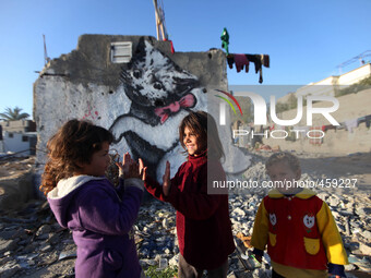 Palestinian children playing near a mural of a cat, it is assumed that the British street artist Banksy, is seen in the rest of the House wi...