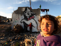Palestinian children playing near a mural of a cat, it is assumed that the British street artist Banksy, is seen in the rest of the House wi...