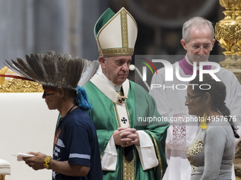 Indigenous peoples, some with their faces painted and wearing feathered headdresses, stand by Pope Francis as he celebrates an opening Mass...