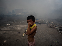 A boy covers his eyes from smoke after a fire broke out in a slum area in Tondo, Manila in the Philippines on April 18, 2020. About 500 fami...