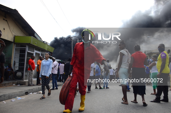 Man of fire fighter walks pass a crowd during the fire outbreak at the Nigerian National Petroleum Corporation (NNPC) petrol station located...