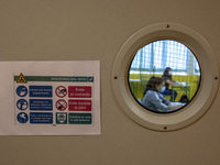 Two students receive a refresher class through a window with a sign indicating the sanitary rules to follow to avoid the coronavirus in Nore...