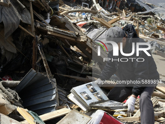 March 20, 2011-Rikuzen Takata, Japan-Native Survivor look his family photo book on debris and mud covered at Tsunami hit Destroyed city in R...