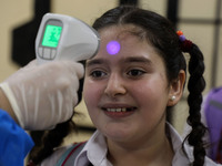 A Palestinian staff member checks a student temperature in the rosary sisters school gaza , on the first day of a new school year, as Palest...