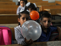 Palestinian students holding balloons sit in a classroom at a United Nations-run school as a new school year begins as Palestinians ease the...