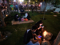 An Iranian couple use their smartphones as they sit next to candles on a street-side while attending a ceremony to commemorate Ashura, in no...