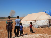 Displaced Syrians watch smoke billowing after Russian air strikes near their tent in the town of Patenta, west of the city of Maarat Misrin,...