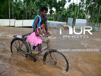 A man carries his daughter on a bicycle as he wades through a flooded area, following heavy rainfall, in Nagaon  in the northeastern state o...