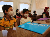Syrian students wearing protective masks sit on their seats during the first day of the school year in a camp for displaced people near the...