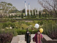 Two Iranian women who one of them carrying balloons walk along an area as long-range surface to surface Missiles and two satellite carriers...
