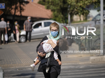 An Iranian woman wearing a protective face mask carrying her kid as she crosses an avenue. in northern Tehran while the new coronavirus (COV...