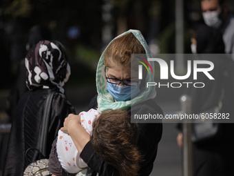 An Iranian woman wearing a protective face mask carrying her kid as she crosses an avenue in northern Tehran while the new coronavirus (COVI...