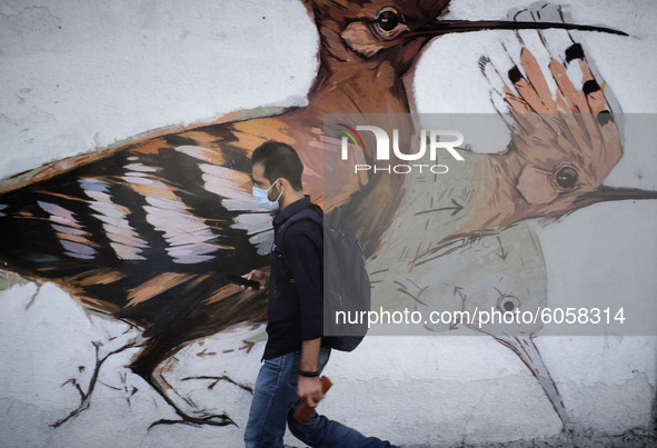 An Iranian man wearing a protective face mask walks past a mural in northern Tehran while the new coronavirus (COVID-19) disease rapid risin...