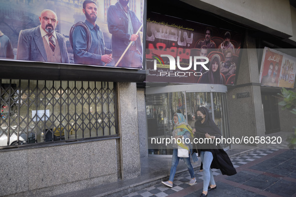 Two Iranian women wearing protective face masks walks past a closed cinema in northern Tehran following the new coronavirus (COVID-19) disea...
