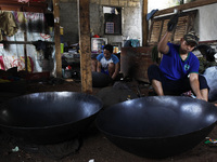 A craftsman works on making a steel wok made of steel plate in the home industry, 