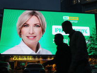 People walk next to a screen of a shopping mall that displays an election campaign advertisement of Iryna Vereshchuk a Ukrainian lawmaker fr...