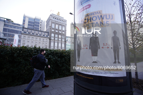 A man wearing a face mask walks past a poster urging people to keep distance in Warsaw, Poland on October 8, 2020. The ministry of health on...