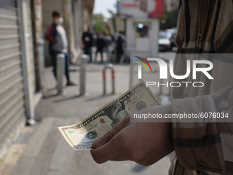 An Iranian man holds U.S. banknote as he stands on a street side near a currency exchange shop in Tehran’s business district on October 10,...
