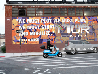 A view of a person riding a Revel scooter in front of a billboard in Williamsburg, Brooklyn. New York  City enters Phase 4 of re-opening fol...