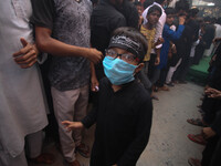 A shiite muslim boy wearing a protective mask as a protective measure against Covid 19 corona virus, as others mourn during a religious proc...