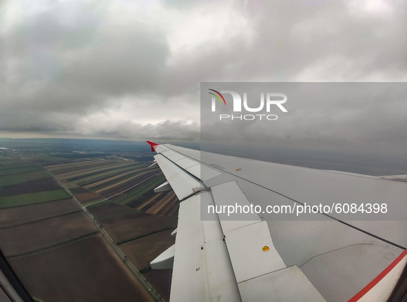 Wing view from the window of the plane with clouds and Austrian fields during the flight. Flying with Lauda Airbus A320 airplane with regist...