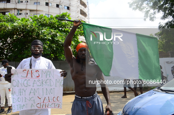  Youths of ENDSARS protesters display the Nigerian flag and a placard in a crowd in support of the ongoing protest against the harassment, k...
