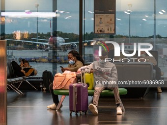 Passengers with facemask sitting infront of the window with aircraft in the background. Passengers wearing facemasks, face shields, gloves a...