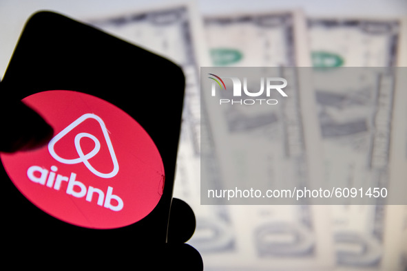 In this photo illustration a Airbnb logo is displayed on a smartphone screen and Dollars bills as background on a computer screen in Athens,...