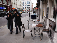 A man and woman with face masks walk past empty tables outside a pub on Cranbourn Street in London, England, on October 16, 2020. London is...