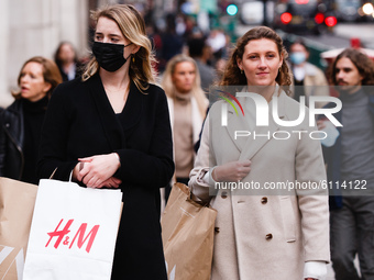 A woman wearing a face mask waits with bags of clothes shopping at a pedestrian crossing on Regent Street in London, England, on October 22,...