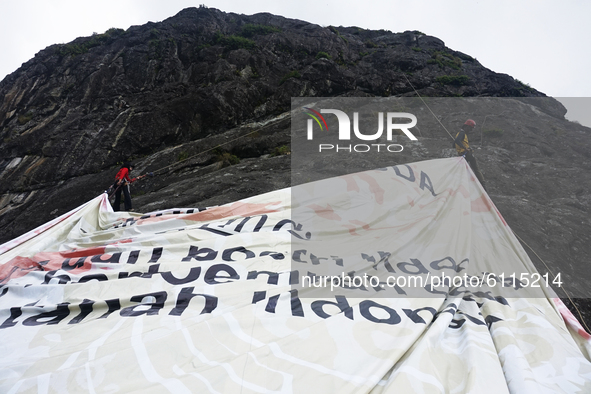 Two teenagers climbing a cliff to fly a large banner with the words Soempah Pemoeda on the Serelo Hill Cliff, Lahat Regency, South Sumatra P...