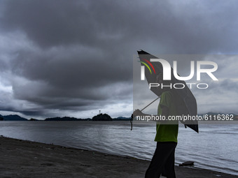 A boy holding an umbrella in the banks of Brahmaputra river as dark clouds gather in the sky, in Guwahati, India on 23 October 2020. (