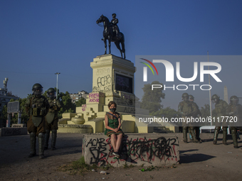 An older adult woman sits in the middle of Plaza Dignidad (former plaza Italia), while being harassed and intimidated by riot police of cara...