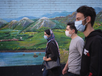 Iranian youth wearing protective face masks to prevent themselves of infection by the new coronavirus disease (COVID-19) walk past a mural i...