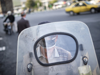 An Iranian motorcyclist wearing a protective face mask to prevent himself of infection by the new coronavirus disease (COVID-19) looks on as...